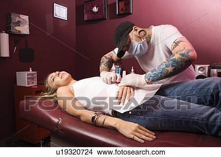 Man giving young woman naval piercing. View Large Photo Image Picture - Man giving young woman naval piercing.. Fotosearch