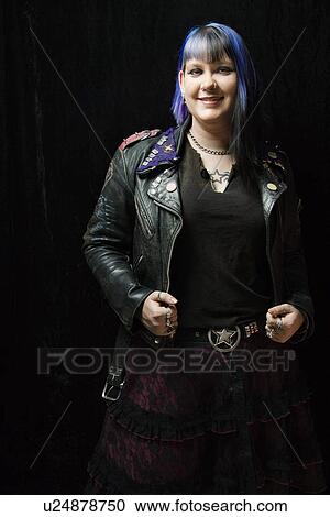 Stock Image - Portrait of smiling Caucasian woman with blue hair and black leather jacket standing against black background.. Fotosearch