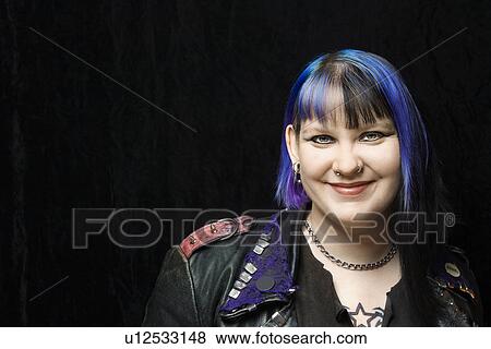 Stock Photo - Portrait of smiling Caucasian woman with blue hair and black leather jacket against black background.. Fotosearch