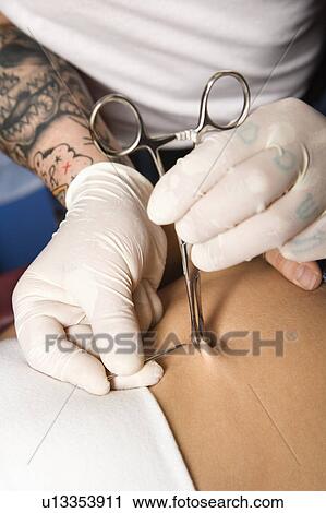 Stock Image - Skin held in piercing tool as needle is ready to go in to pierce naval. Fotosearch