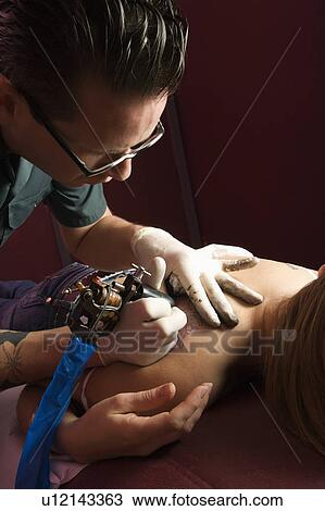 Stock Image - Tattoo artist tattooing woman. Fotosearch