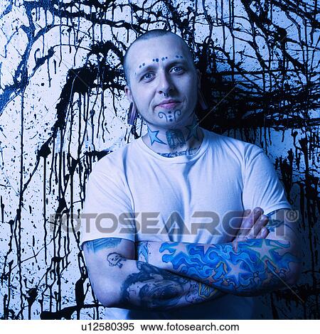 Stock Photography - Tattooed and pierced man standing against paint splattered background.. Fotosearch