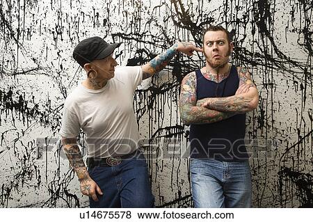 Stock Photo - Two Caucasian tattooed men standing against paint splattered background.. Fotosearch