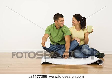 Attractive couple sitting on home floor with coffee cups looking at house plans and smiling at each other. View Large Photo Image Stock Photograph - Attractive couple sitting on home floor with coffee cups looking at house plans and smiling at each other.. Fotosearch
