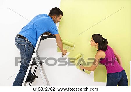 Stock Image - Attractive young adult couple painting interior wall of house.. Fotosearch