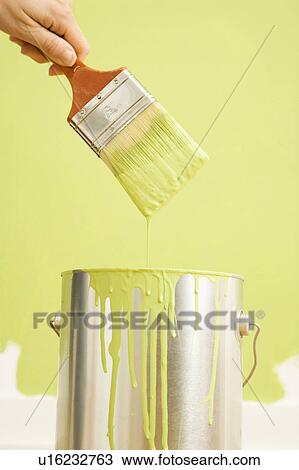Stock Image - Female hand holding paintbrush over paint can. Fotosearch