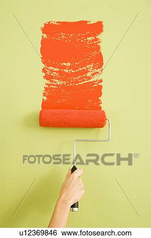 Stock Photograph - Hand painting a green wall with a red paint roller. Fotosearch