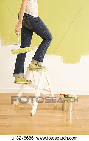 Stock Photograph - Legs of woman climbing stepladder holding paint roller. Fotosearch