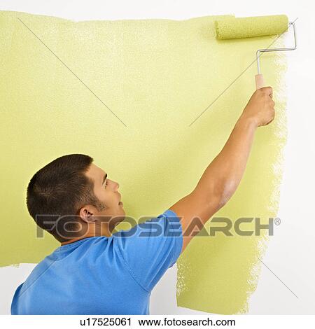 Stock Image - Man painting over white wall with green paint using paint roller.. Fotosearch