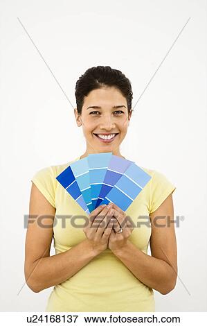 Stock Photo - Pretty smiling woman holding paint sample cards in front of white wall.. Fotosearch