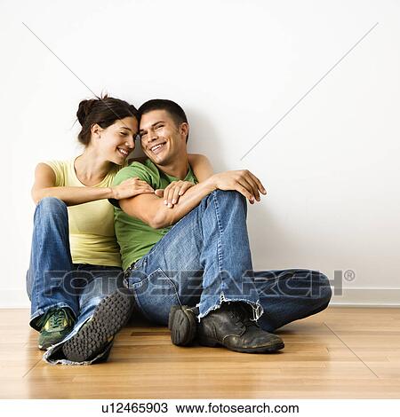 Stock Image - Smiling attractive couple sitting on floor in home.. Fotosearch