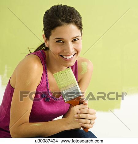 Picture - Woman kneeling in front of partially painted wall. Fotosearch