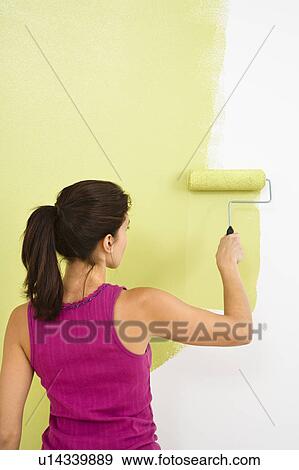 Stock Photo - Woman painting interior wall of home with paint roller. Fotosearch