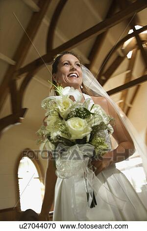 Stock Image - Bride holding bouquet leaving a church. Fotosearch