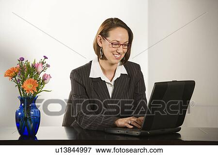 Stock Photo - Businesswoman sitting at desk smiling with laptop computer. Fotosearch
