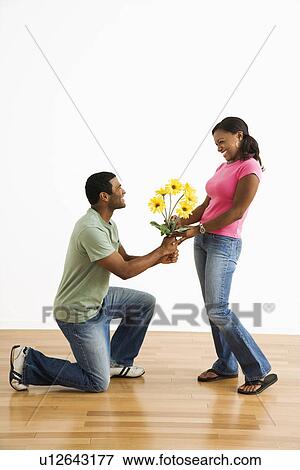 Stock Photo - Male giving pretty female a bouquet of yellow flowers while on bended knee.. Fotosearch