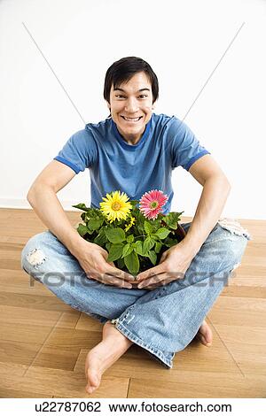 Stock Image - Man sitting holding pot of gerbera daisies.. Fotosearch