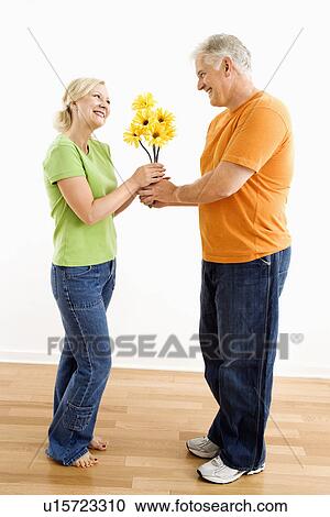 Stock Image - Middle-aged man giving woman bouquet of yellow flowers.. Fotosearch