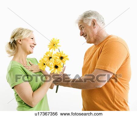 Stock Photograph - Middle-aged man giving woman bouquet of yellow flowers.. Fotosearch