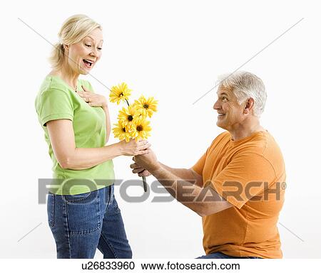 Stock Image - Middle-aged man on bended knee giving woman bouquet of yellow flowers.. Fotosearch