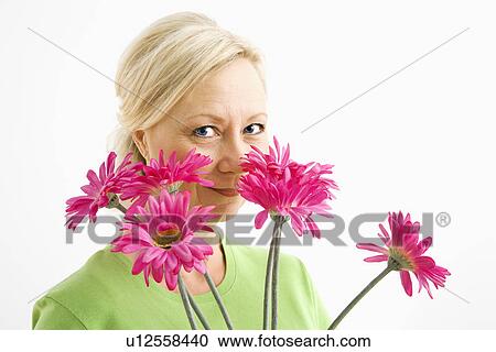 Stock Image - Portrait of smiling adult blonde woman looking over bouquet of pink flowers at viewer.. Fotosearch