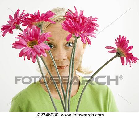 Stock Image - Portrait of smiling adult blonde woman looking through bouquet of pink flowers at viewer.. Fotosearch