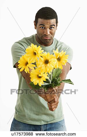 Stock Photo - Pouting male holding out bouquet of yellow flowers to unseen person.. Fotosearch