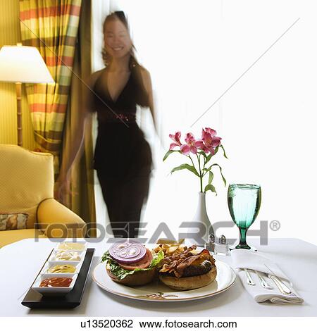 Room service cheeseburger meal with flowers and woman in background View Large Photo Image Stock Image - Room service cheeseburger meal with flowers and woman in background. Fotosearch