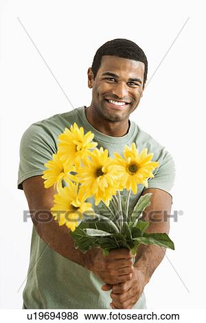 Stock Photo - Smiling male holding out bouquet of yellow flowers to unseen person.. Fotosearch