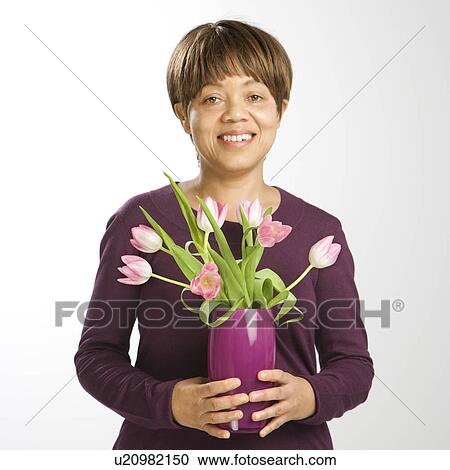 Stock Image - Smiling woman holding vase of pink tulips. Fotosearch