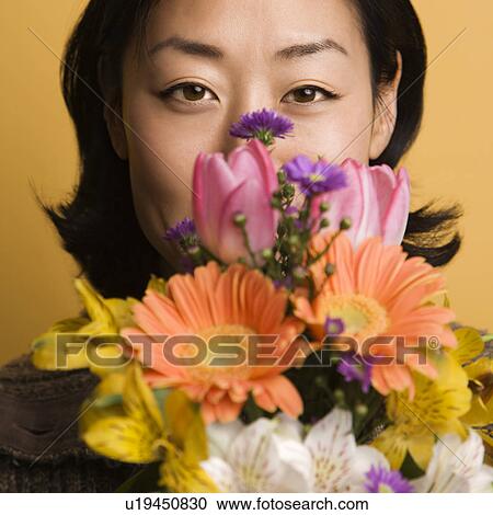 Stock Image - Woman holding bouquet of flowers up to face. Fotosearch