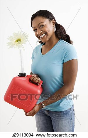 Picture - Young adult female holding gas can with flower in it's nozzle.. Fotosearch