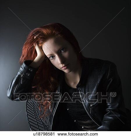 Stock Image - Portrait of pretty redhead young woman sitting in chair resting head on hand. Fotosearch