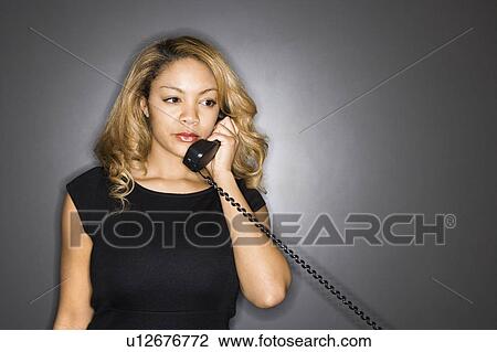 Stock Image - Woman holding telephone receiver to ear. Fotosearch