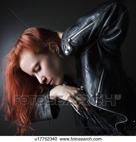 Stock Image - Woman wearing leather jacket hanging over back of chair. Fotosearch