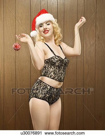 Stock Image - Attractive Caucasian woman wearing santa hat and holding holiday ornament.. Fotosearch