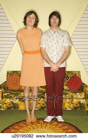 Stock Image - Caucasian mid-adult couple wearing retro clothes standing in room decorated with vintage furniture.. Fotosearch