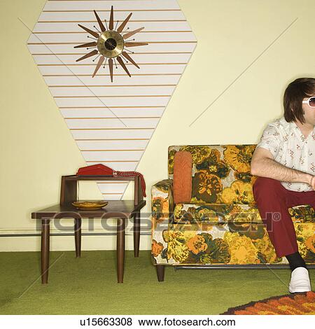 Caucasian mid-adult man sitting on colorful retro sofa wearing sunglasses in room with vintage decor. View Large Photo Image Stock Photo - Caucasian mid-adult man sitting on colorful retro sofa wearing sunglasses in room with vintage decor.. Fotosearch