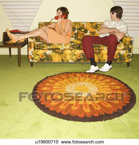 Stock Image - Caucasian mid-adult woman on phone while Caucasian mid-adult man wearing sunglasses watches from sofa.. Fotosearch