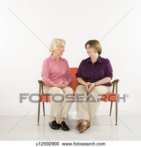 Stock Image - Caucasian middle aged woman and senior woman sitting conversing.. Fotosearch
