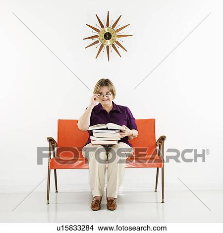 Picture - Caucasian middle aged woman sitting holding stack of books.. Fotosearch