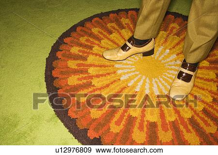 Stock Photo - Close-up of Caucasian mid-adult male feet in vintage shoes against sunburst rug.. Fotosearch