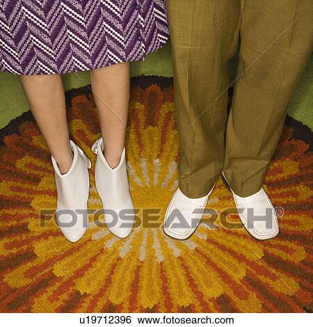Stock Photograph - Close-up of Caucasian mid-adult male and female legs in vintage clothing against sunburst rug.. Fotosearch