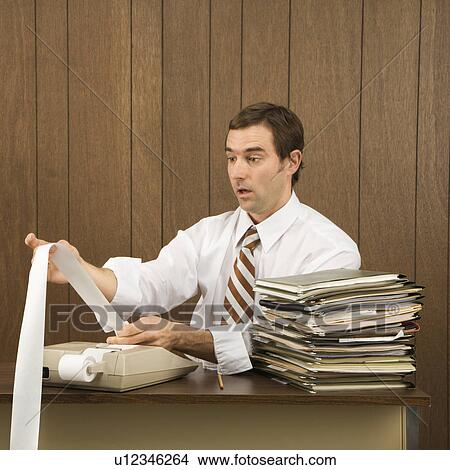 Picture - Mid-adult Caucasian male holding printout from calculator in office setting.. Fotosearch