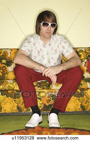Stock Photo - Portrait of Caucasian mid-adult man wearing sunglasses sitting on colorful retro sofa.. Fotosearch
