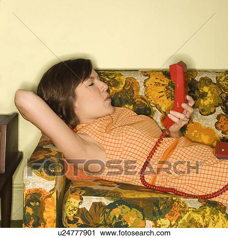 Pretty Caucasian mid-adult woman lying on colorful retro sofa with arm behind head holding red telephone receiver. View Large Photo Image Stock Image - Pretty Caucasian mid-adult woman lying on colorful retro sofa with arm behind head holding red telephone receiver.. Fotosearch
