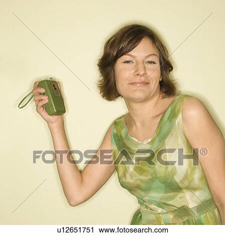 Stock Image - Pretty Caucasian mid-adult woman wearing green vintage dress with handheld radio smiling at viewer.. Fotosearch