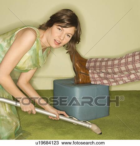 Unhappy pretty Caucasian mid-adult woman kneeling and vaccuuming carpet around male feet resting on foot stool. View Large Photo Image Stock Image - Unhappy pretty Caucasian mid-adult woman kneeling and vaccuuming carpet around male feet resting on foot stool.. Fotosearch