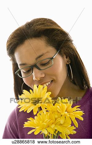 Stock Photo - African American mid adult woman wearing glasses smelling bouquet of Gerbera dasies.. Fotosearch