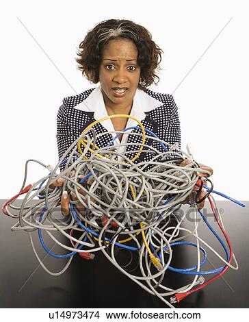 Picture - Businesswoman holding bundle of tangled computer cords with overwhelmed look on her face.. Fotosearch